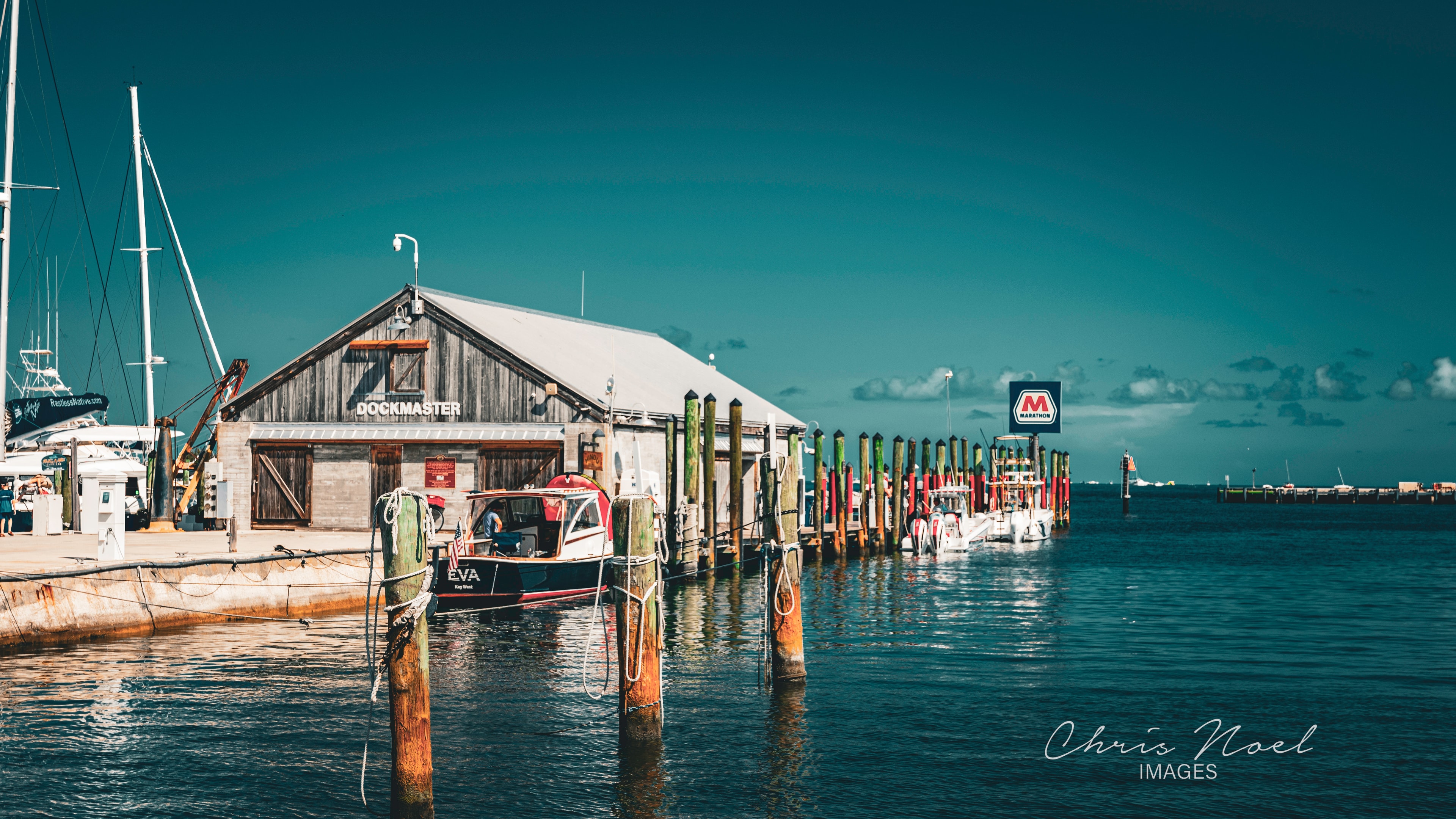 Coastal marina with boats and dockmaster building in vivid teal and turquoise tones