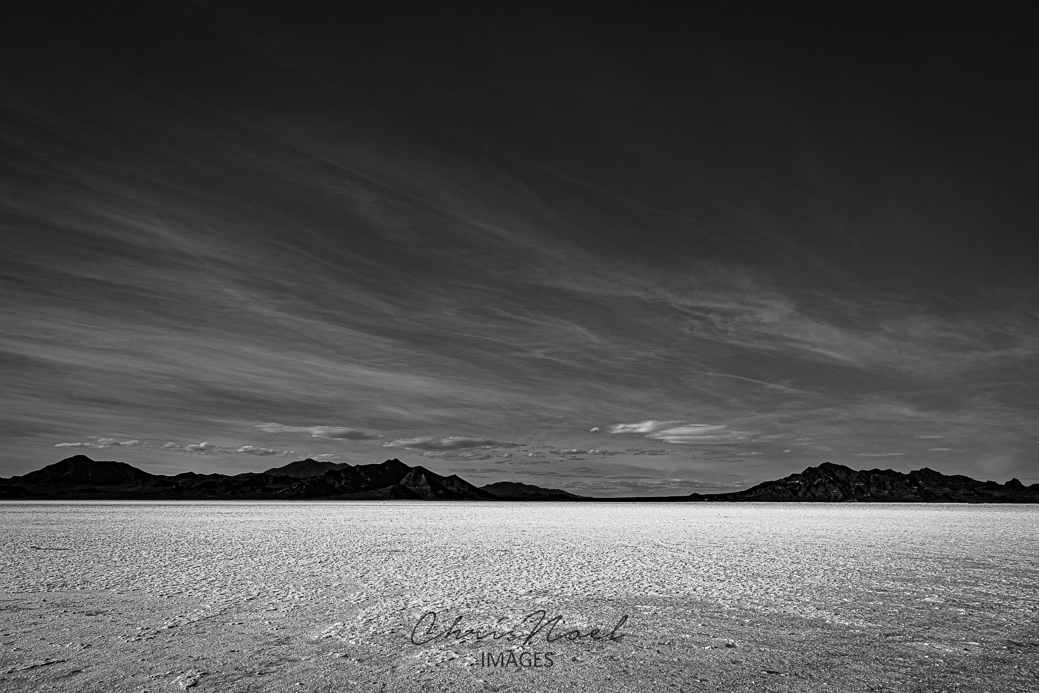 Black and white desert salt flat with dramatic streaked sky and distant mountains